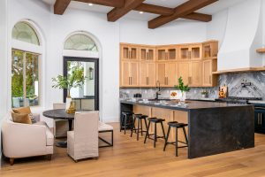 A kitchen with light wood cabinets, a dark island, and bar stools next to a round breakfast nook by tall arched windows.