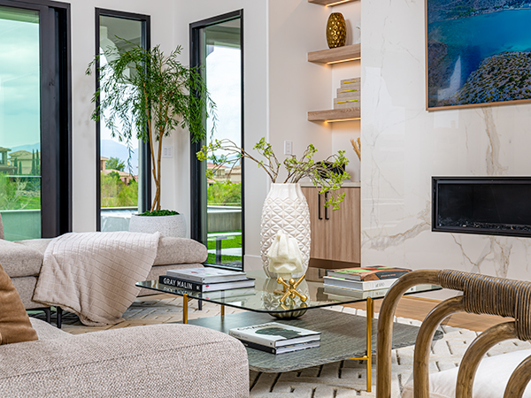 A modern living room with a glass coffee table, cozy neutral seating, decorative vases, and large windows bringing in natural light.