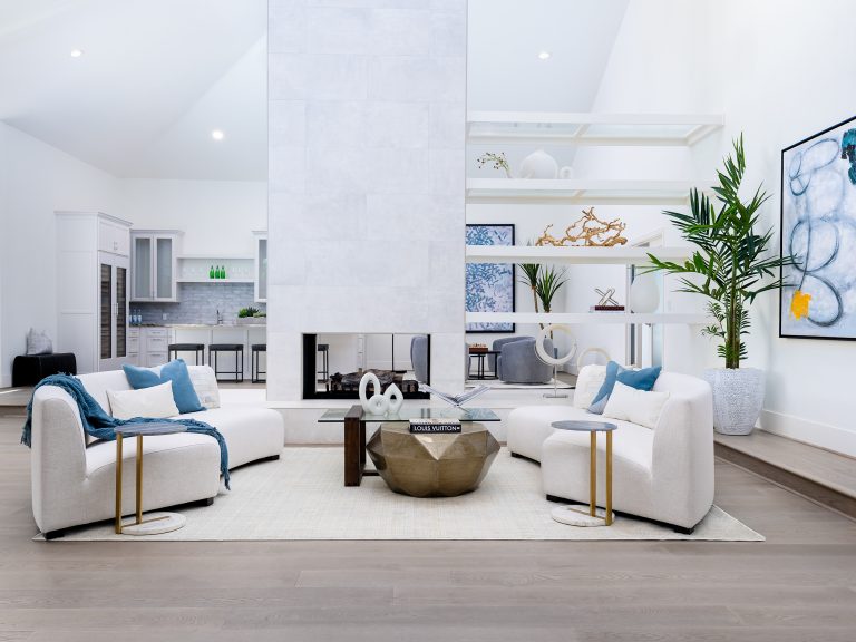 A bright living area featuring a tall double-sided fireplace, curved white sofas, and open shelving that divides the space.