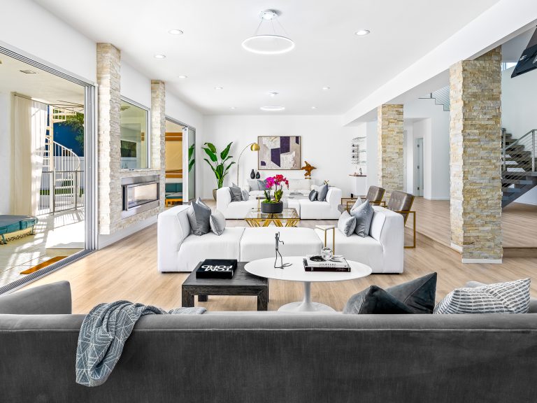 An open living room with white modular seating, stone columns, and large sliding doors leading to a pool.