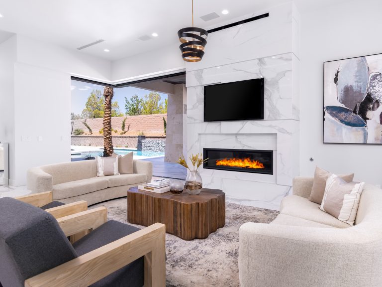 A living room featuring a marble fireplace, curved sofa, and wooden coffee table, with sliding doors opening to a pool area.