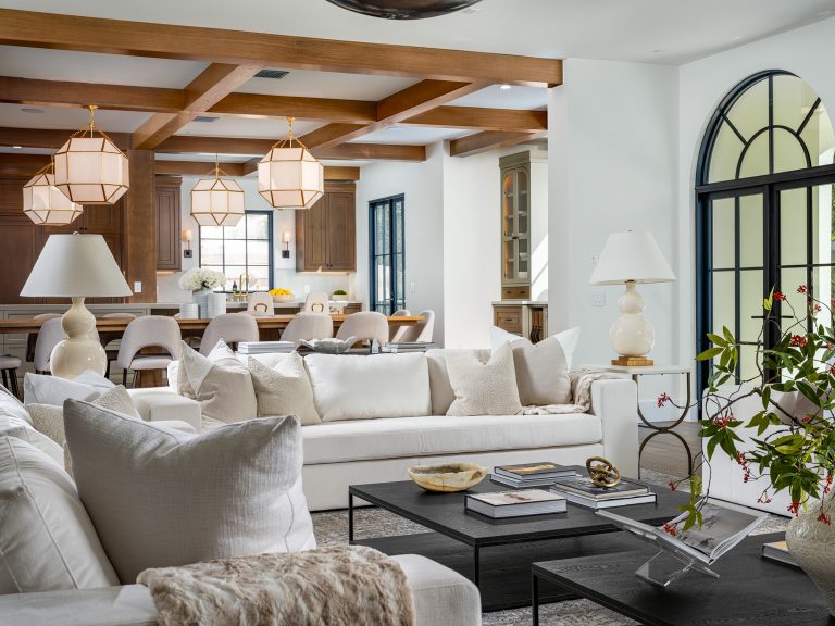 Refined Living Home Staging in a bright, open living space featuring white sofas, warm wood beams, and a spacious kitchen backdrop.