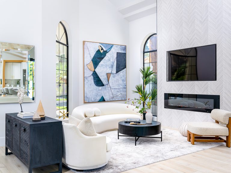 A bright living area with an arched window, a curved white sofa, and a herringbone-pattern fireplace showcasing a modern electric fireplace.