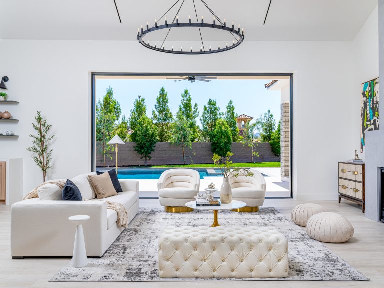 Luxurious Comfort Home Staging with a white sofa, two plush accent chairs, and a tufted ottoman opening to a backyard pool view.