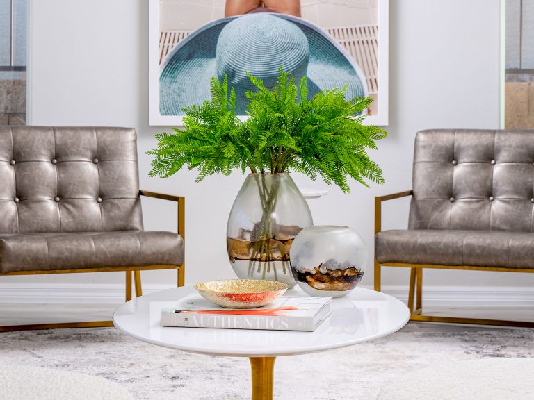 A bright seating arrangement with tufted metallic chairs and a round white table holding glass vases and lush greenery.