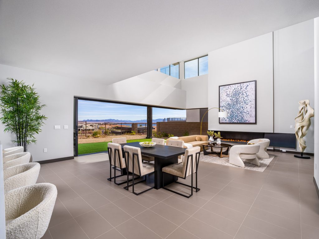 A spacious living and dining area with a large sliding glass wall, overlooking desert scenery and featuring neutral, modern furnishings.