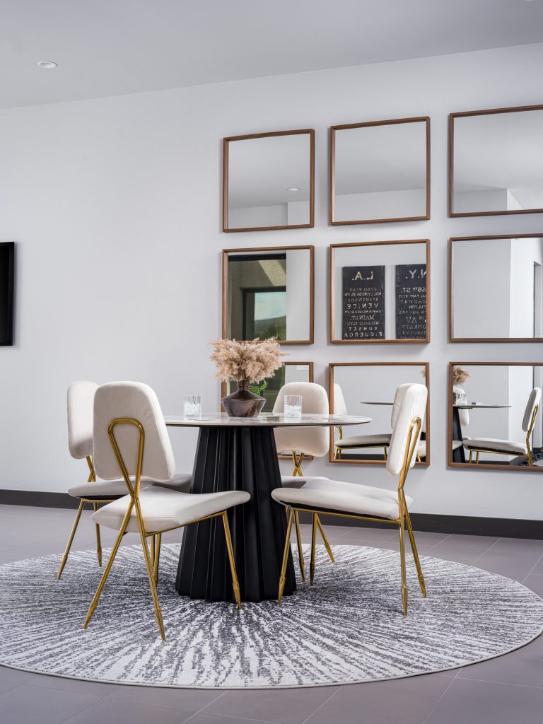 A round black table with velvet chairs on a circular rug, set before a wall of mirrors.