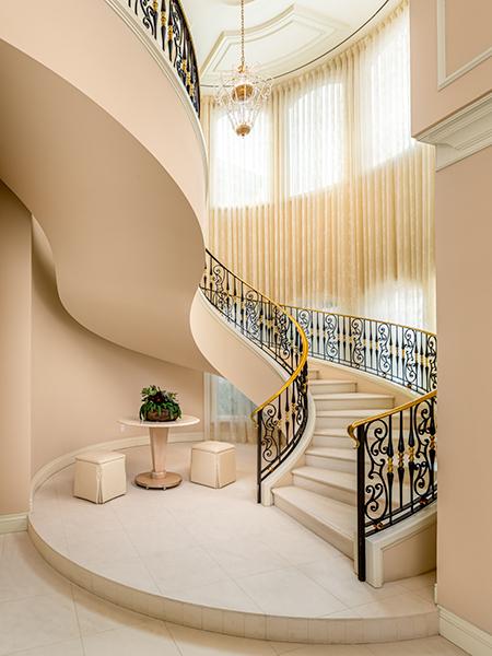 A stunning curved staircase with ornate wrought iron railings, elegant drapery, and a luxurious chandelier in a grand foyer.