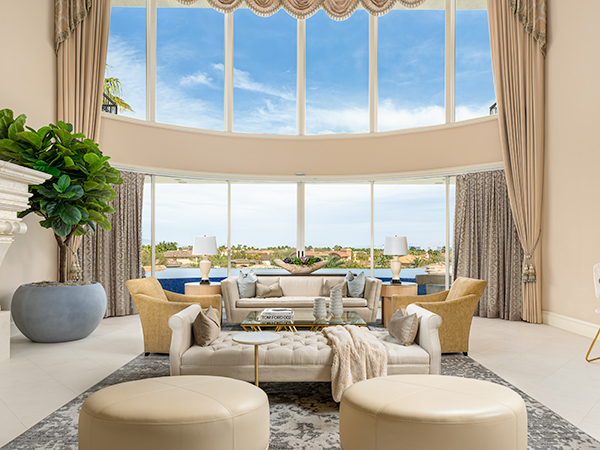A luxurious living room with a grand window, elegant drapery, plush seating, and a sophisticated neutral color palette.