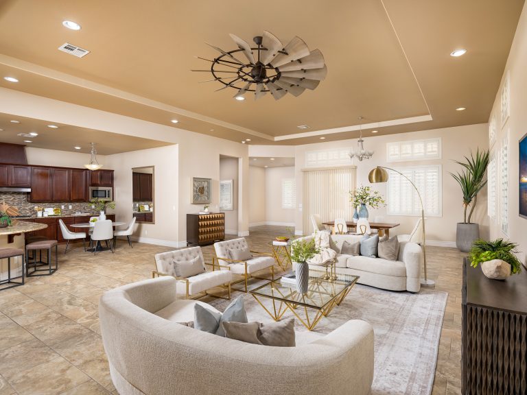 A spacious open-concept area with curved sofas, gold accent tables, and a warm-toned kitchen and dining space in the background.